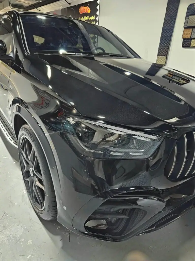 فنيون محترفون يقومون بتركيب أفلام حماية PPF بدقة عالية على سيارة سوداء